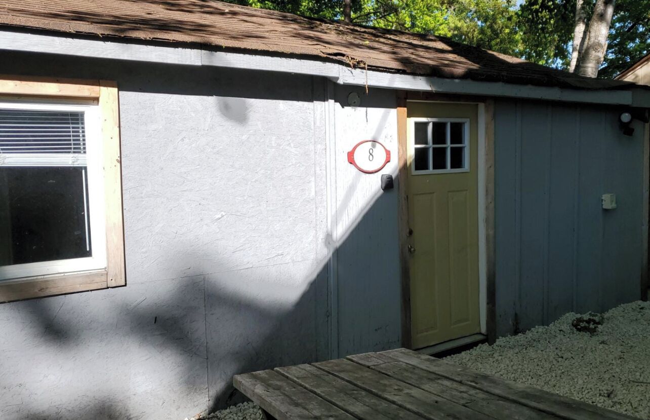 A small, single-story building with a yellow door and a window with a wooden frame.
