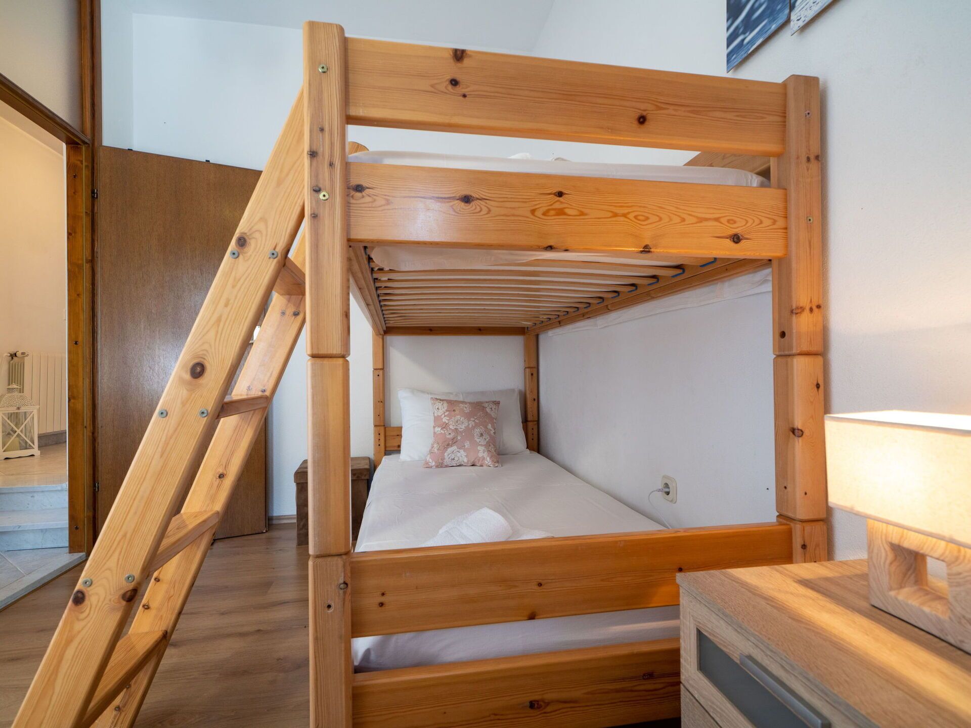 Uma cama beliche de madeira com escada, mesa de cabeceira e abajur.