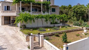 Una casa de dos pisos con fachada de piedra, un balcón y un jardín con muro y portón de piedra.