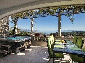 Een terras met een jacuzzi, eettafel met stoelen en uitzicht op zee en bergen.