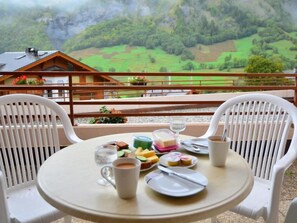 A table set with food and drinks on a balcony overlooking a mountainous landscape.