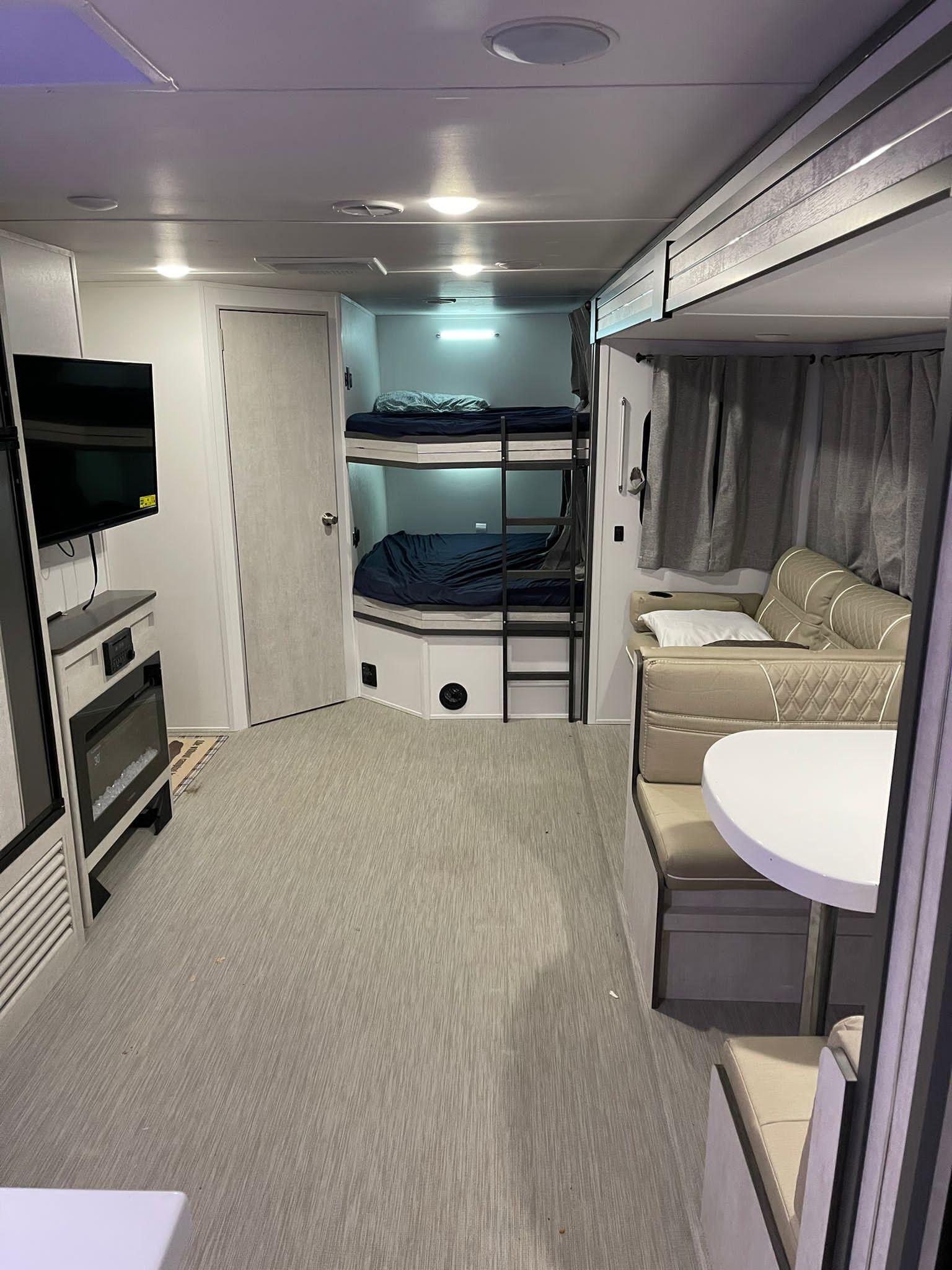 A compact, well-lit room with bunk beds, a television, a small table, and a sofa.