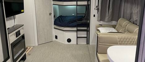 A compact, well-lit room with bunk beds, a television, a small table, and a sofa.