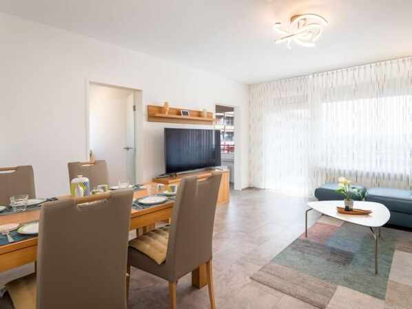 A modern living room with a dining area, a flat-screen TV, and a sofa.