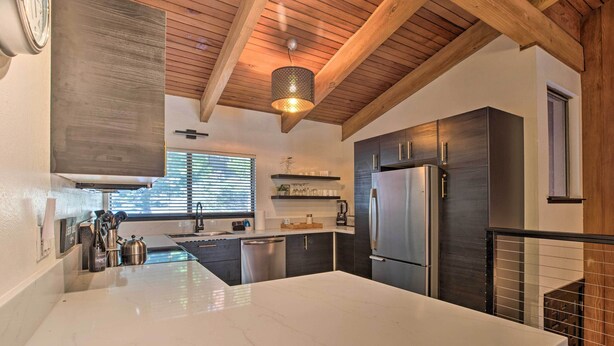 A modern kitchen with a large island, stainless steel appliances, and wooden ceiling beams.