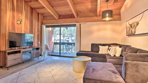 A modern living room with a wooden ceiling, a large TV, a sofa, and a sliding glass door leading to an outdoor area.
