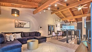 A spacious living room with a sectional sofa, a coffee table, and a dining area with a high ceiling and exposed beams.