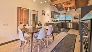 A modern kitchen with wooden beams, a dining area with a glass table and white chairs, and a kitchen island with a sink and stove.