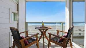 Un balcon avec deux chaises en bois et une petite table, donnant sur une plage.