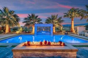 A swimming pool with a fire feature, surrounded by palm trees and a stone wall.