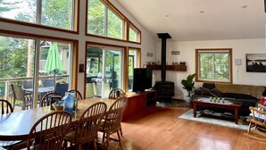 Een ruime woonkamer met een hoge plafond, grote ramen, een open haard, een televisie en een gezellige zithoek.