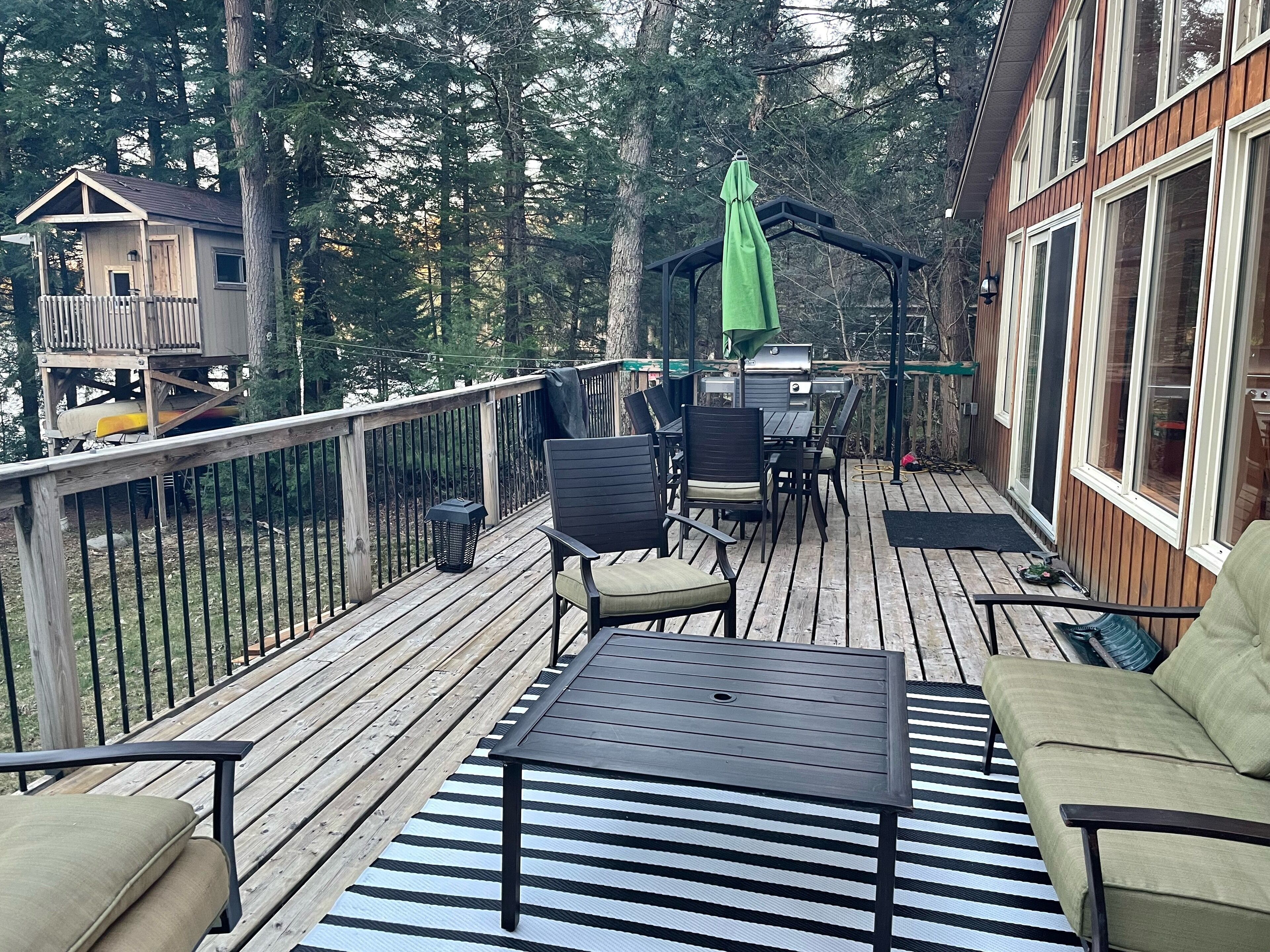 En træterrasse med udendørs møbler, herunder et bord, stole og en grill.