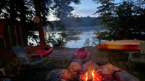 Een terras aan het meer met een vuurkorf, kajaks en Adirondack-stoelen.