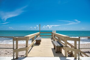 A wooden pier leading to a beach with benches and a railing.