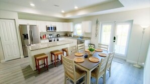 A modern kitchen with white cabinets, a central island, and a dining area with a wooden table and chairs. - Vero's Cove  (Vero Beach)