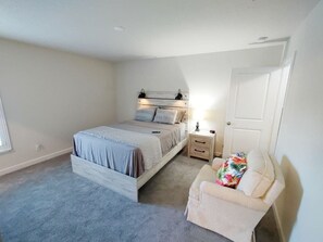 A bedroom with a bed, bedside tables, a chair, and a door. - Vero's Cove  (Vero Beach)