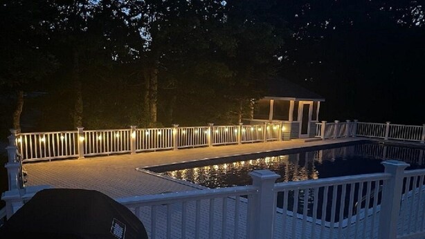 A deck with a pool, surrounded by a white fence and illuminated by string lights. - RUSH SALE- Family Discount! Weeks of Aug 22-Sept 5th!!! (Dennis)