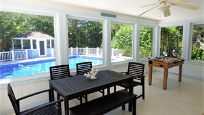 A sunlit patio with a pool view, a table with chairs, and a foosball table. - RUSH SALE- Family Discount! Weeks of Aug 22-Sept 5th!!! (Dennis)