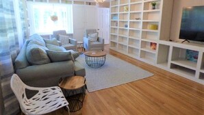 A living room with a sofa, chairs, a coffee table, a TV, and built-in shelving. - RUSH SALE- Family Discount! Weeks of Aug 22-Sept 5th!!! (Dennis)
