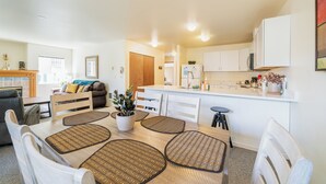A modern kitchen with white cabinets, a central island, and a dining area with a wooden table and white chairs. - Wander in to Alpine, a basecamp for your adventure!! (Leavenworth)