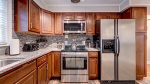 Uma cozinha moderna com armários de madeira, eletrodomésticos de aço inoxidável, bancadas de granito e painel de azulejos.