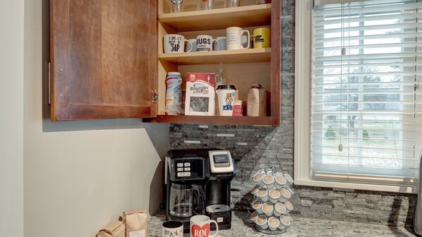 A kitchen with a wooden cabinet, a coffee maker, and a window with blinds.