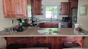 A kitchen with wooden cabinets, granite countertops, a stainless steel refrigerator, and a window providing natural light.