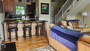 A modern kitchen with wooden cabinets, a bar area with stools, and a staircase leading to a loft bedroom.