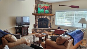 A living room with a stone fireplace, leather sofas, a television, and a window with blinds.
