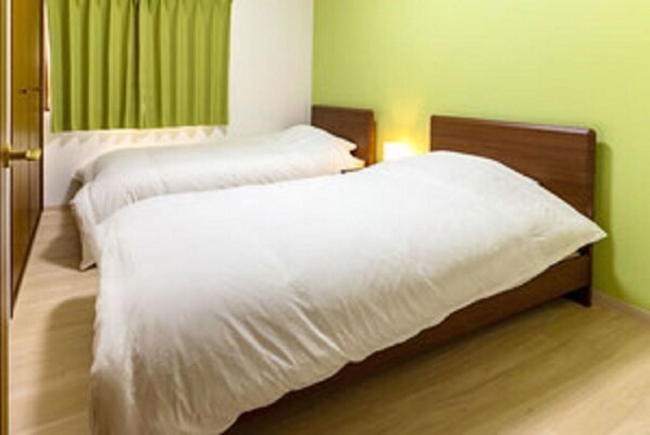 Two single beds with wooden headboards and white mattresses, set against a green wall and wooden floor.
