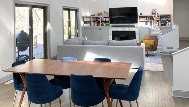 Un vaste espace de vie comprenant une grande table à manger, des chaises bleues, un canapé gris et un téléviseur à écran plat.
