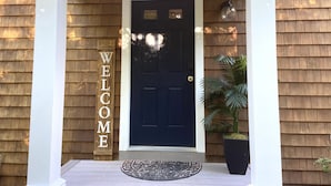 A dark blue door with a welcome sign on the left, a potted plant to the right, and a patterned doormat in front.