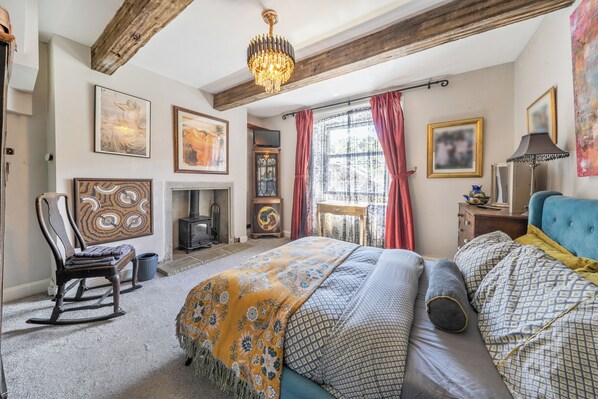 Une chambre à coucher avec un lit, un fauteuil à bascule, une cheminée et des œuvres d’art accrochées aux murs.