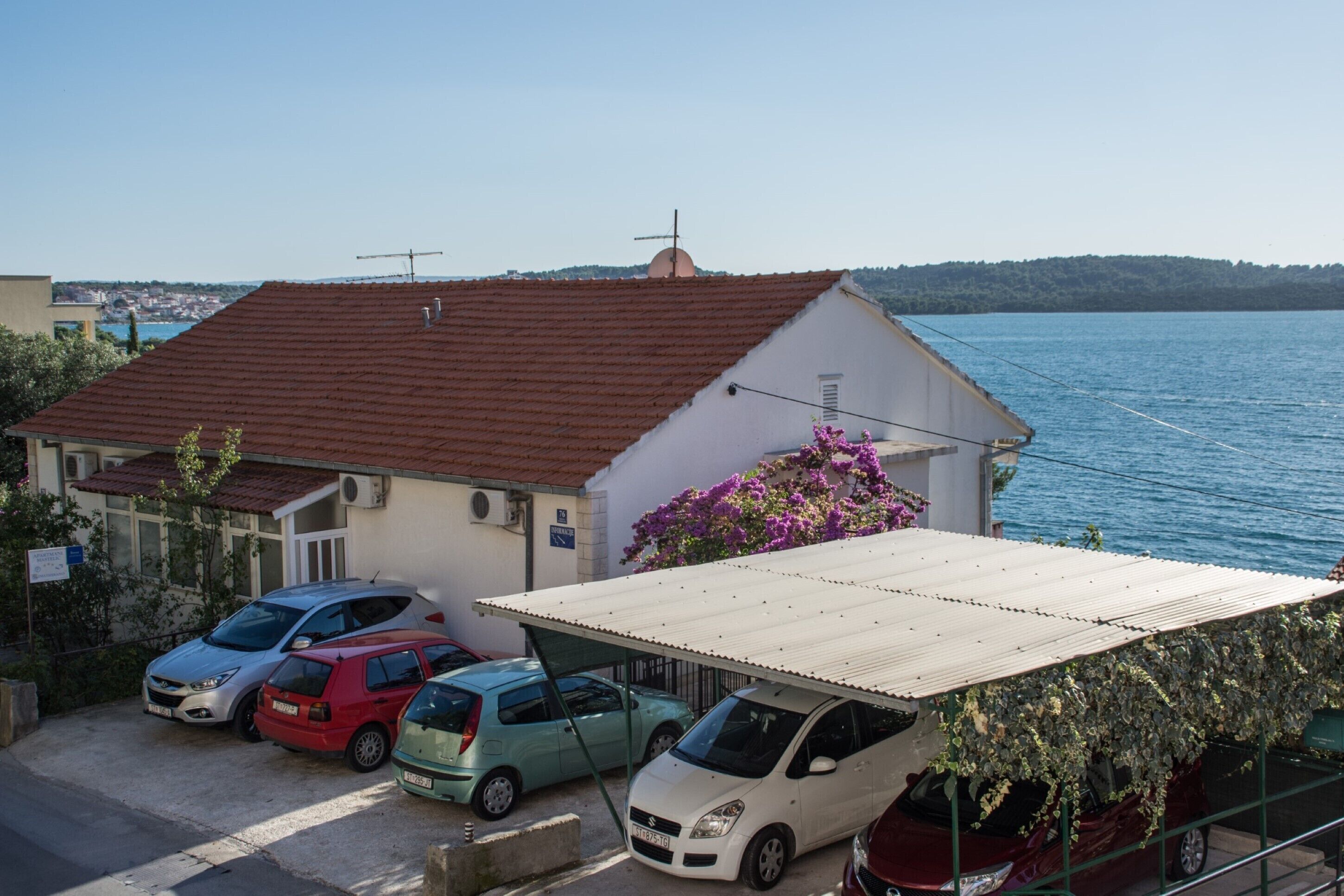 A coastal building with a red-tiled roof, a covered parking area, and a view of the sea.