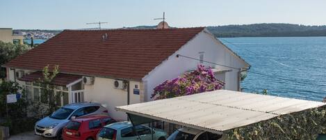 A coastal building with a red-tiled roof, a covered parking area, and a view of the sea.