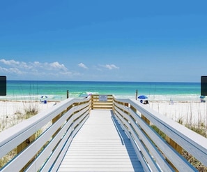 A wooden boardwalk leading to a beach with umbrellas and chairs.