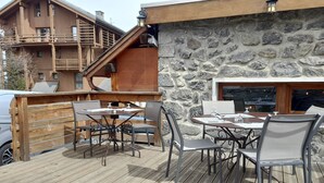 An outdoor patio with wooden tables and chairs, a stone wall, and a wooden deck.