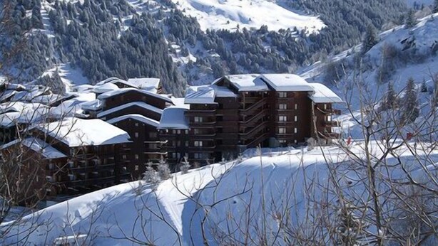 A cluster of multi-story buildings with a snow-covered roof, surrounded by a mountainous landscape.