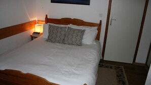 A neatly made bed with a wooden headboard, a bedside lamp, and a framed picture on the wall.