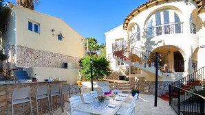 An outdoor patio with a stone table and white chairs, a stone wall, and a staircase leading to a balcony. - Vacation home La Paz by Interhome (Calpe/Calp)