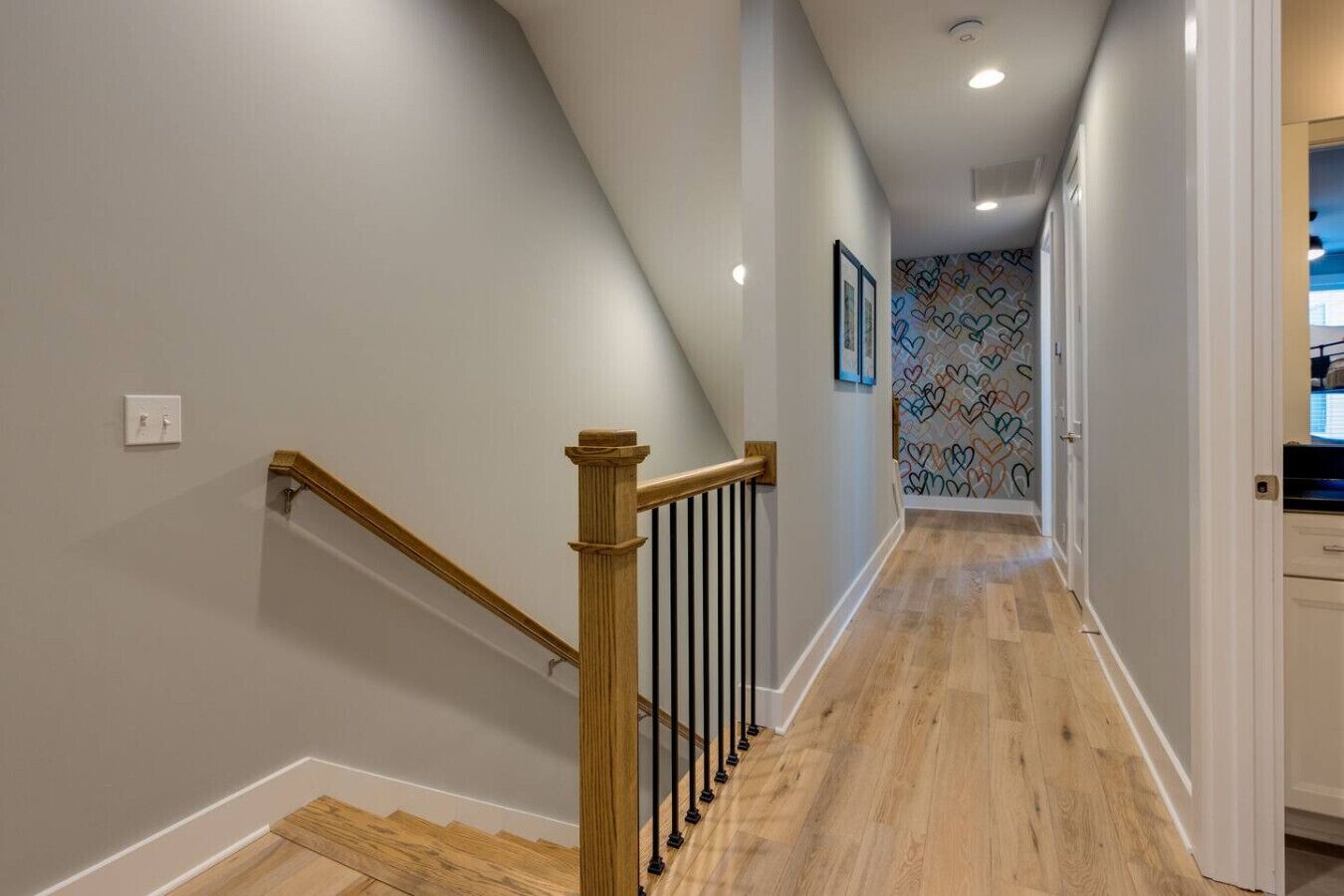 A hallway with wooden flooring, a wooden handrail, and a patterned wall.