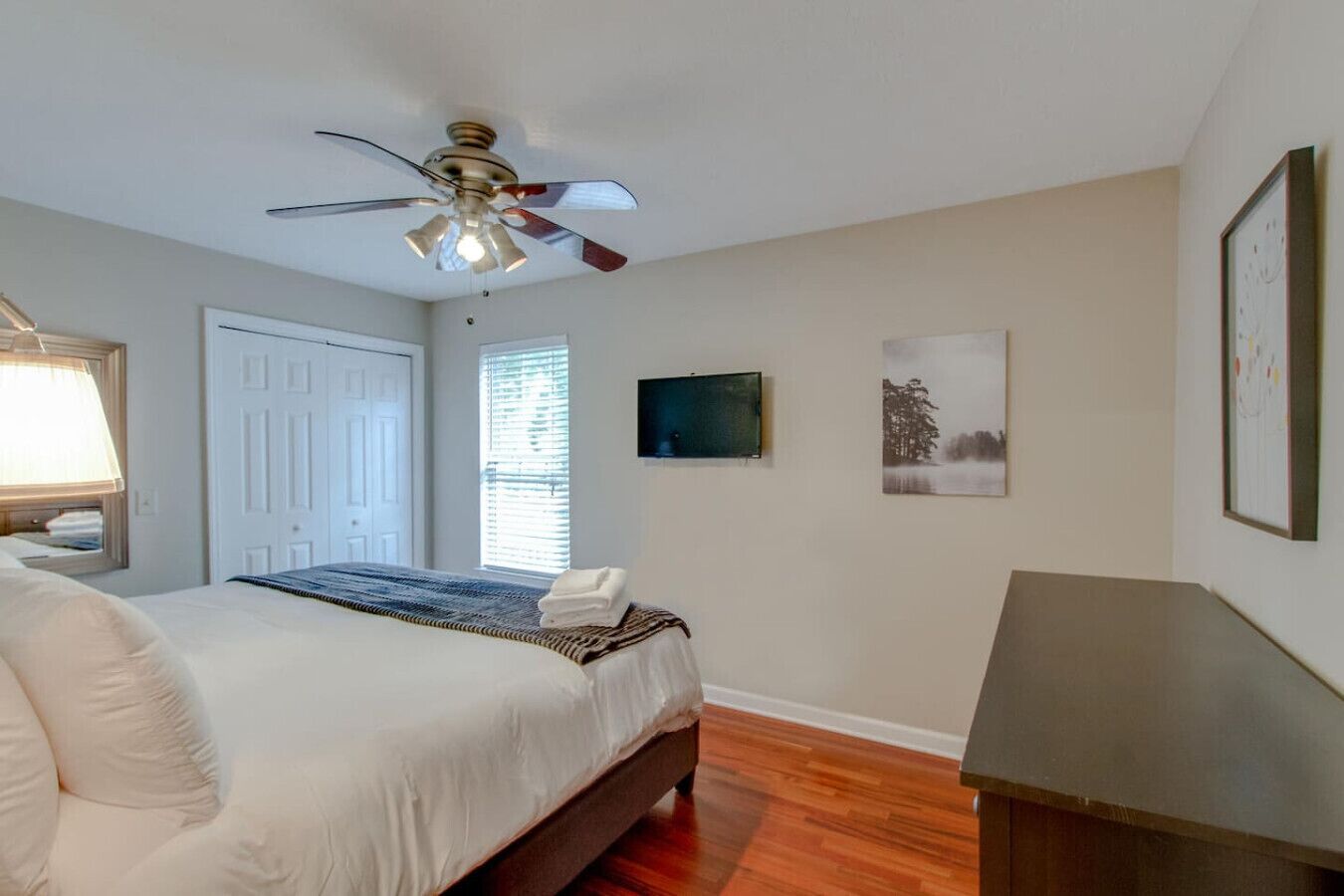 Habitación de hotel con cama, ventilador de techo, ventana con persianas e imagen enmarcada en la pared.