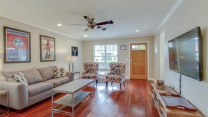 A spacious living room with a sofa, two patterned armchairs, a coffee table, a ceiling fan, and a TV. - Metropolitan City Home - Huge Private Backyard (Nashville)