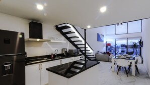Une cuisine moderne aux couleurs noir et blanc, dotée d’un îlot central intégré et d’un escalier menant à un espace repas.