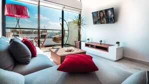 Un salon moderne avec un canapé, des coussins rouges, une table basse, un lampadaire et un tableau accroché au mur.