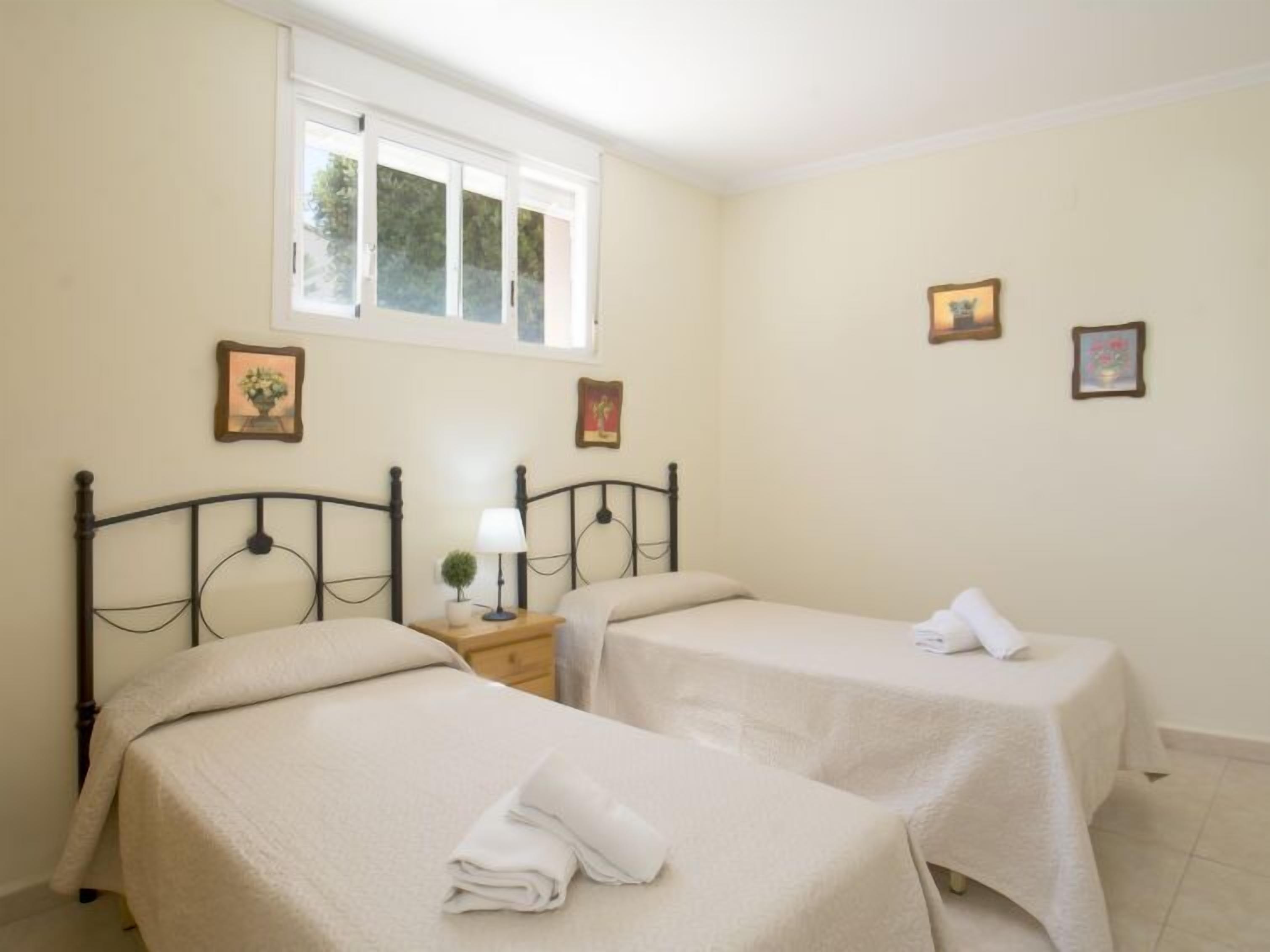 Quarto com duas camas, uma janela e três quadros na parede.
