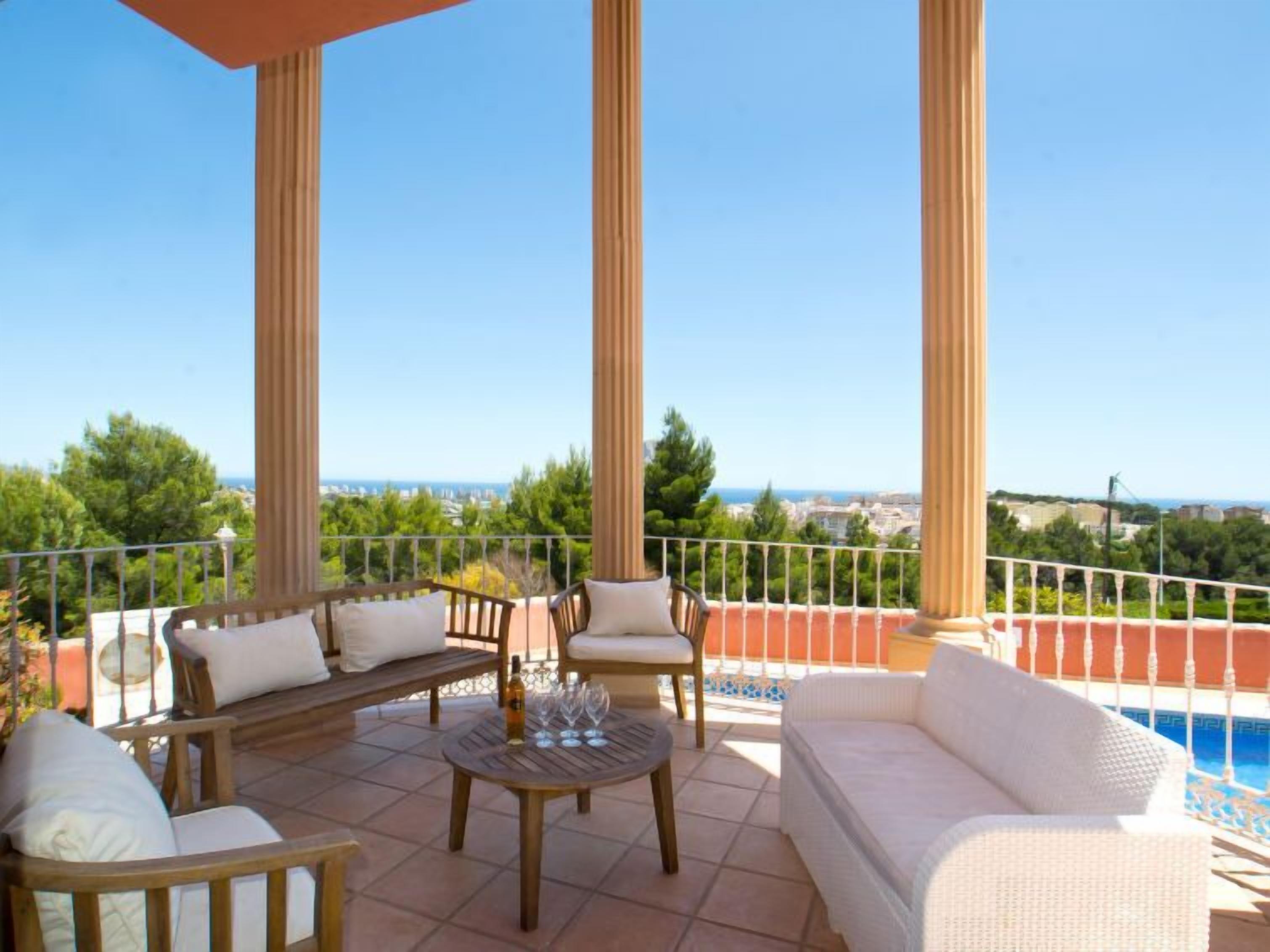 A terrace with a pool, wooden furniture, and a view of the sea.