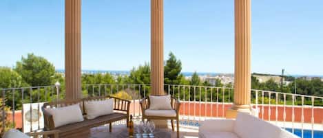 A terrace with a pool, wooden furniture, and a view of the sea.
