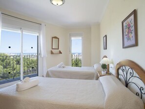 Habitació d'hotel amb dos llits, un balcó amb vistes, una taula petita amb una làmpada i un quadre al mur.