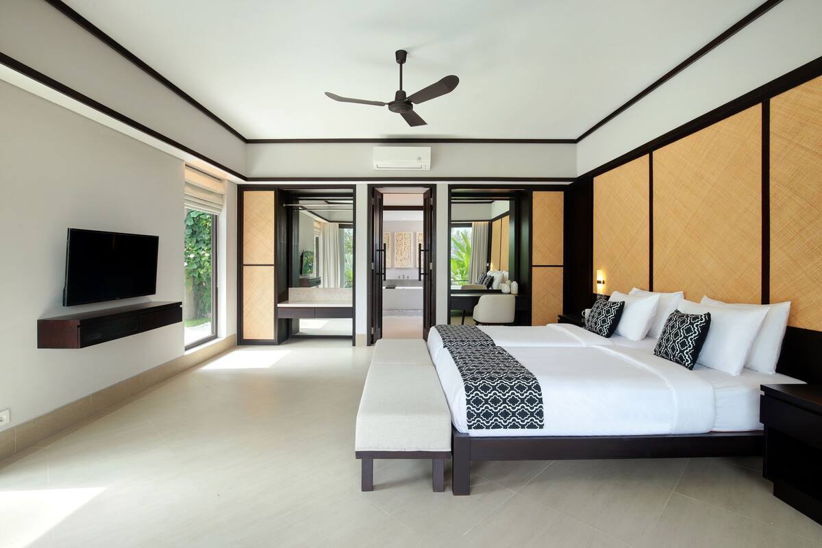 A modern hotel bedroom with a large bed, a ceiling fan, a flat-screen TV, and a view of the outdoors.
